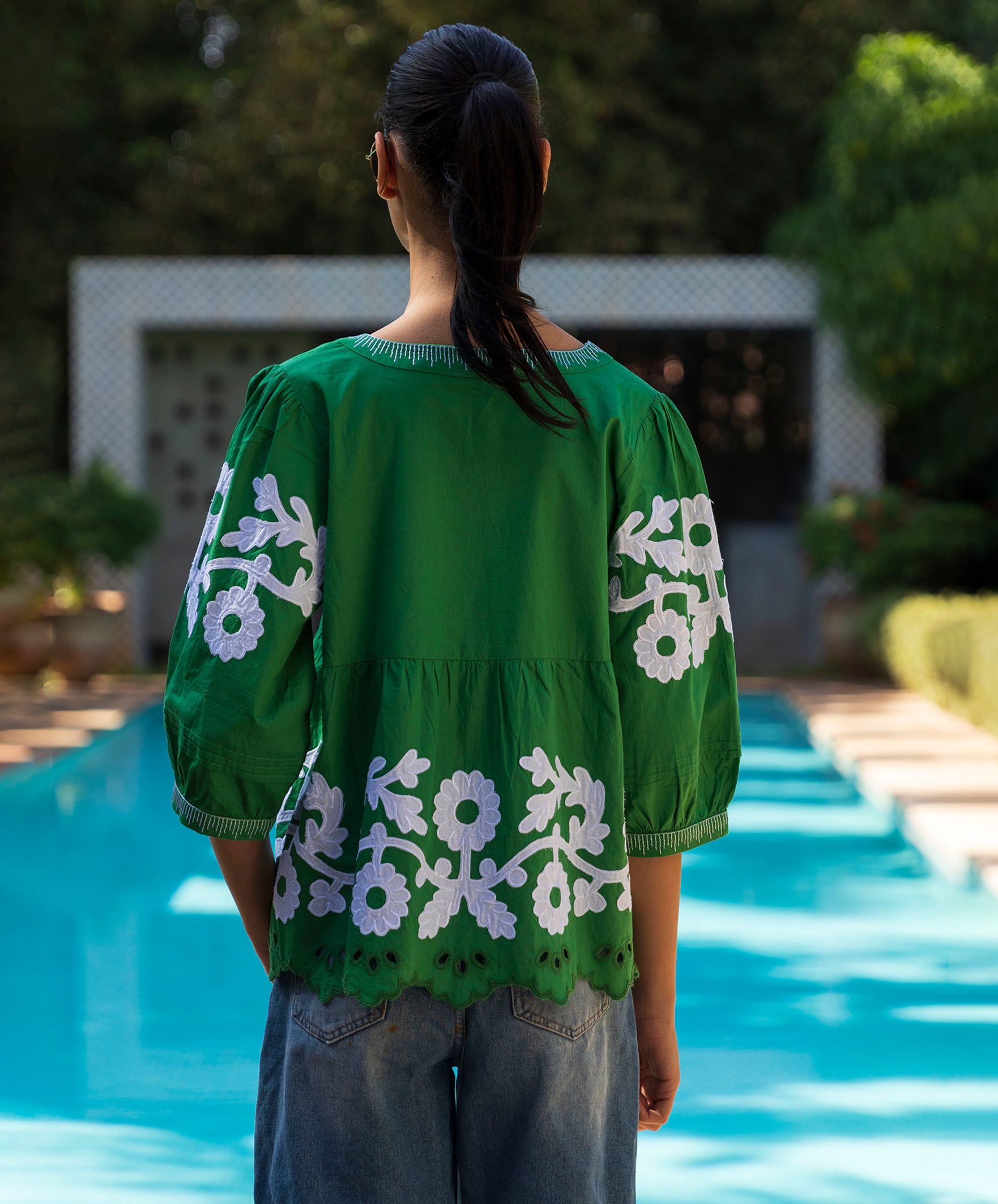 Woman wearing a green blouse with white floral patterns by a pool