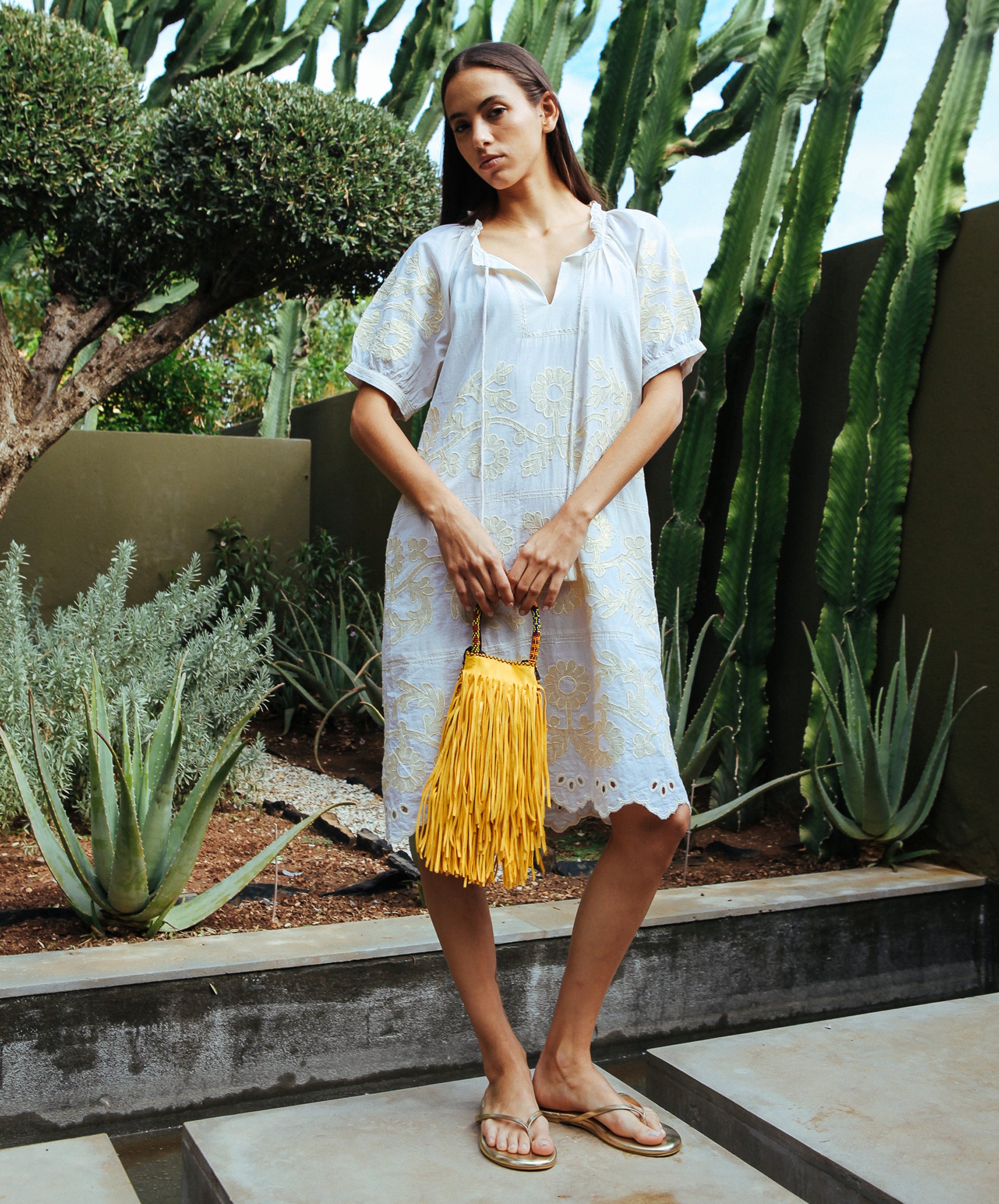 A model stood in a cacti garden wearing a cream Rose and Rose Gloucester cotton dress with gold lurex appliqué decoration.