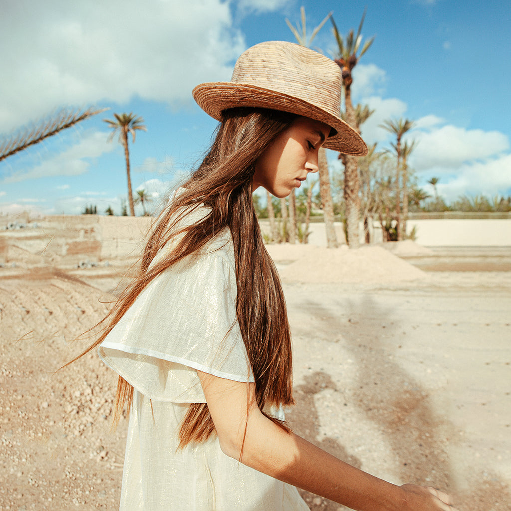 A model  in a hot, sandy location wearing a Rose and Rose Uxbridge gold dress and a straw hat.