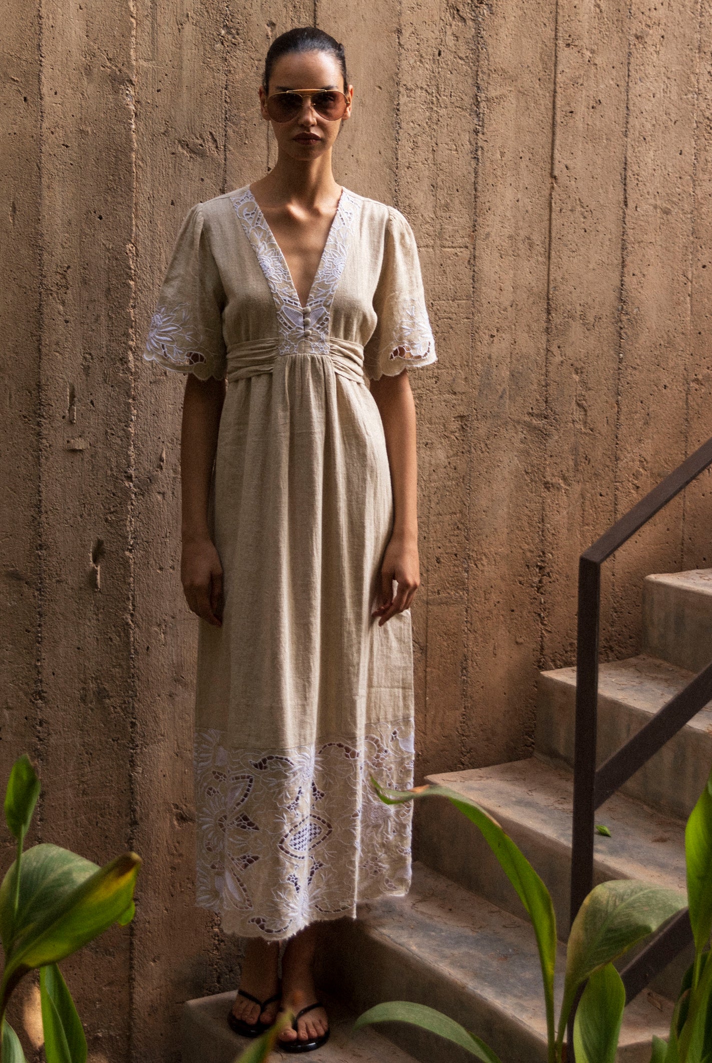 Woman in n embroidered natural linen dress standing on stone steps with a textured wall background