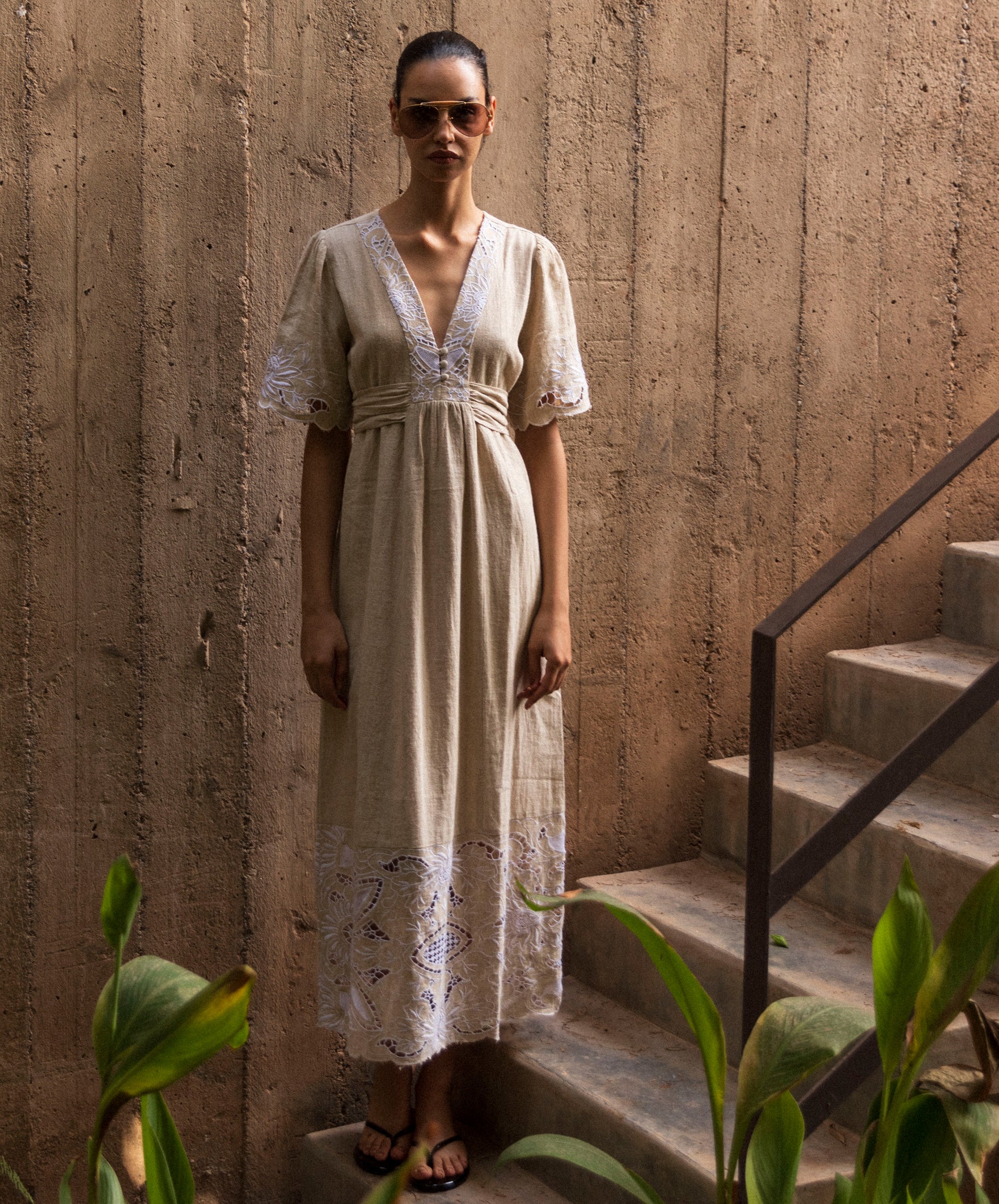 Woman in n embroidered natural linen dress standing on stone steps with a textured wall background