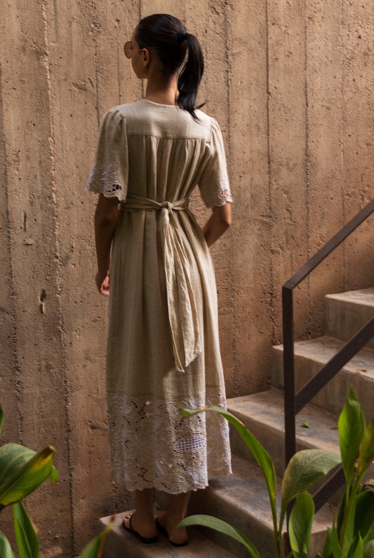Woman in a long, natural linen dress standing on a staircase with a textured wall background