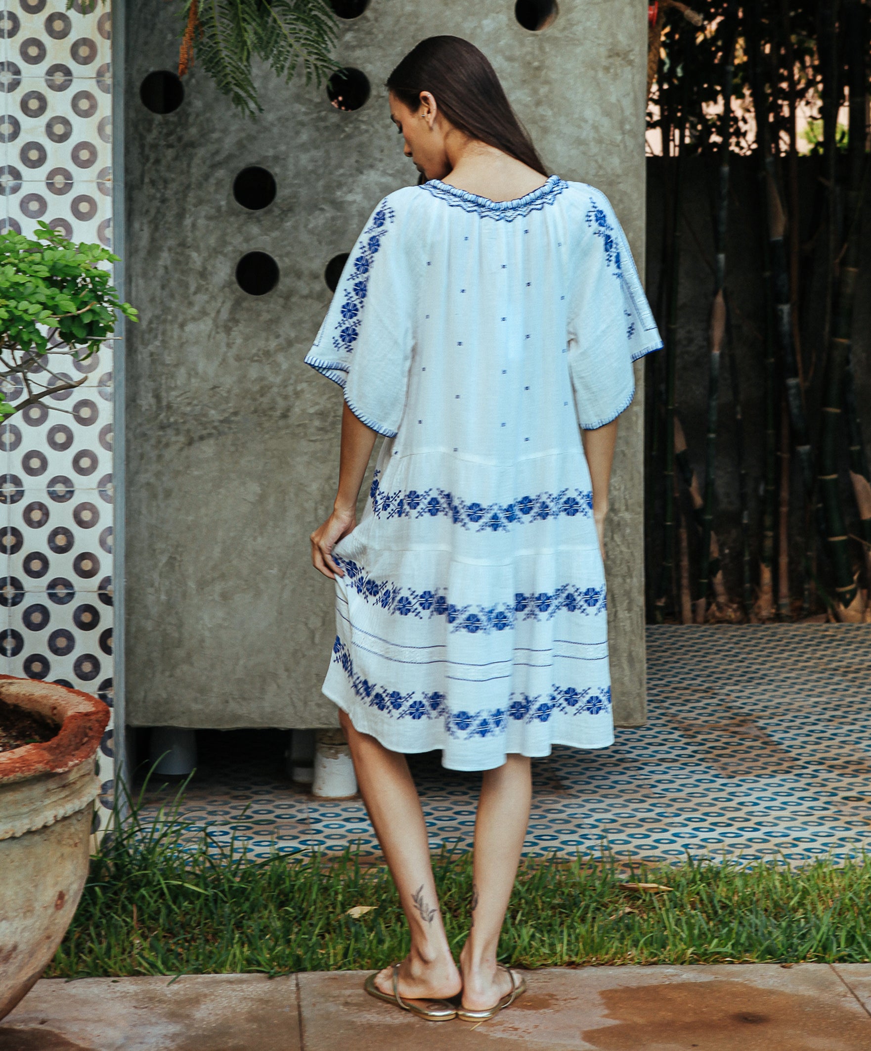 A back view of a model wearing a Rose and Rose Holborn  cotton dress in white with cobalt blue embroidery.