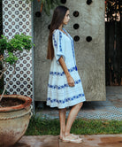 A side view of a model wearing a Rose and Rose Holborn  cotton dress in white with cobalt blue embroidery.
