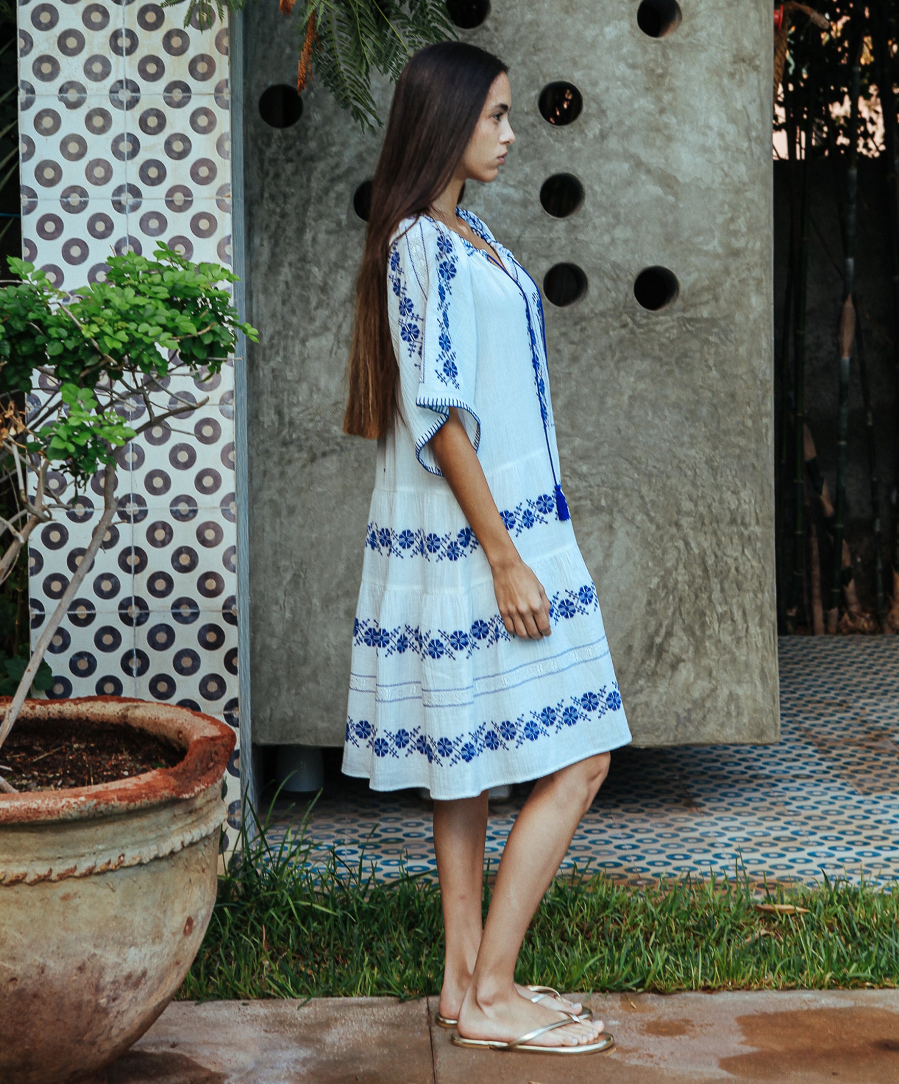 A side view of a model wearing a Rose and Rose Holborn  cotton dress in white with cobalt blue embroidery.
