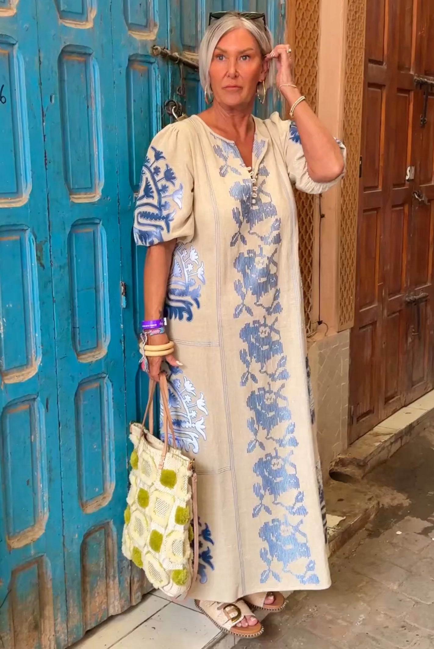 Influencer @simpson.house wearing a Rose natural dress with blue embroidery standing in front of a blue door.