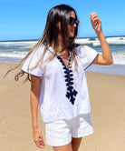  A model stood on a beach wearing a Rose and Rose white Imperia top, white shorts and sunglasses.