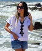 A model stood in front of the sea wearing a Rose and Rose white Imperia top, denim shorts and sunglasses.