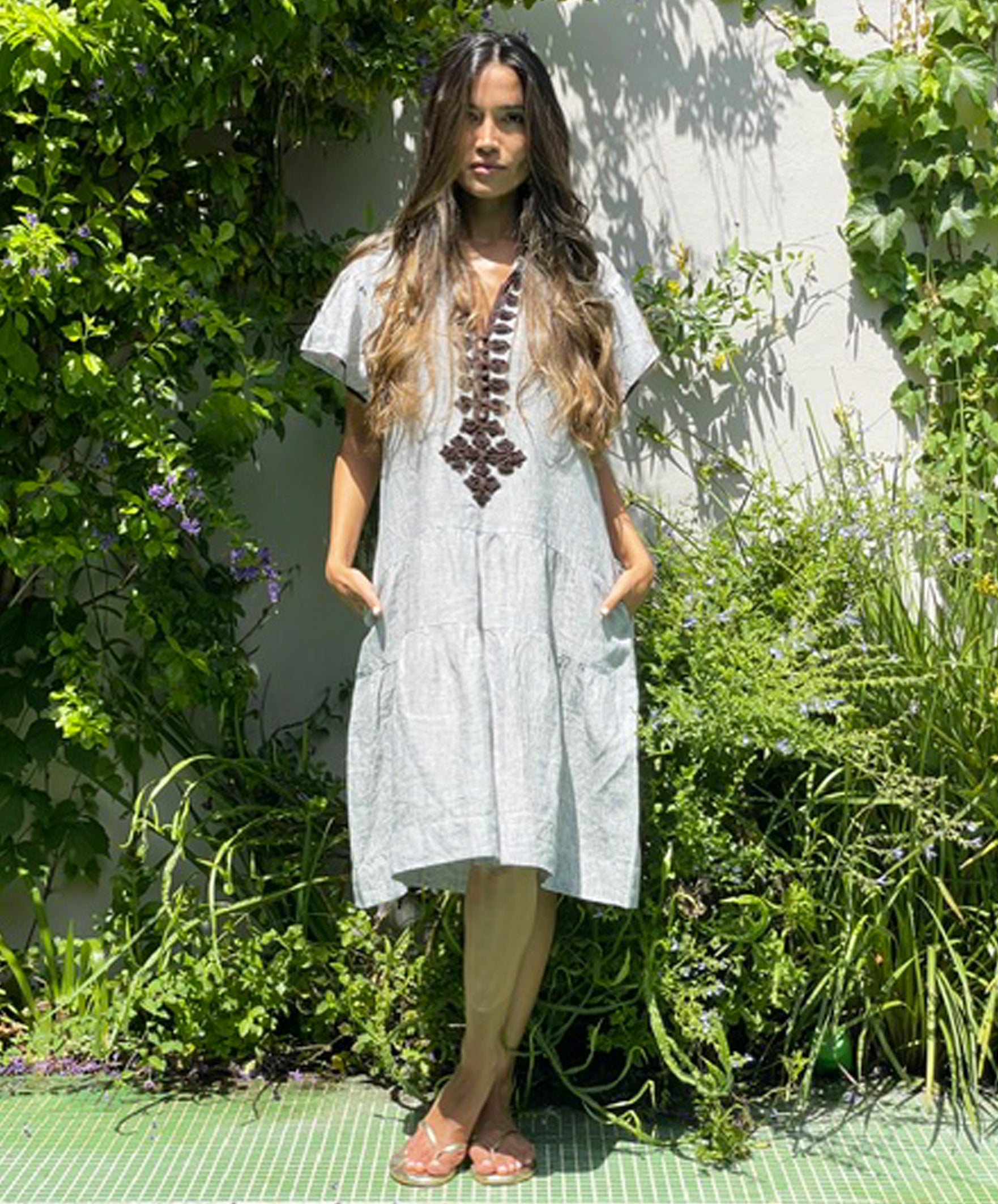 A model stood in a garden wearing a Rose and Rose striped linen Ischia dress.