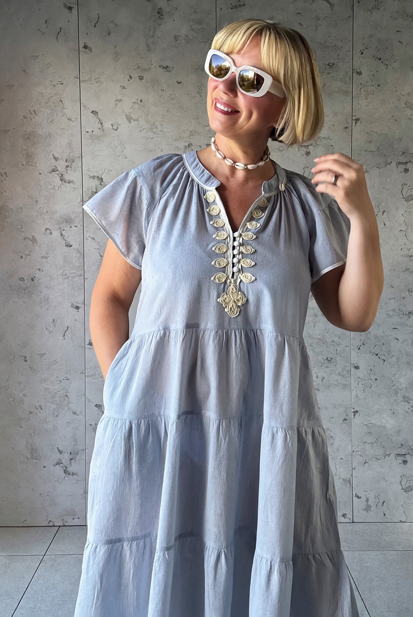 Woman wearing a blue striped dress with white embroidery against a concrete wall.