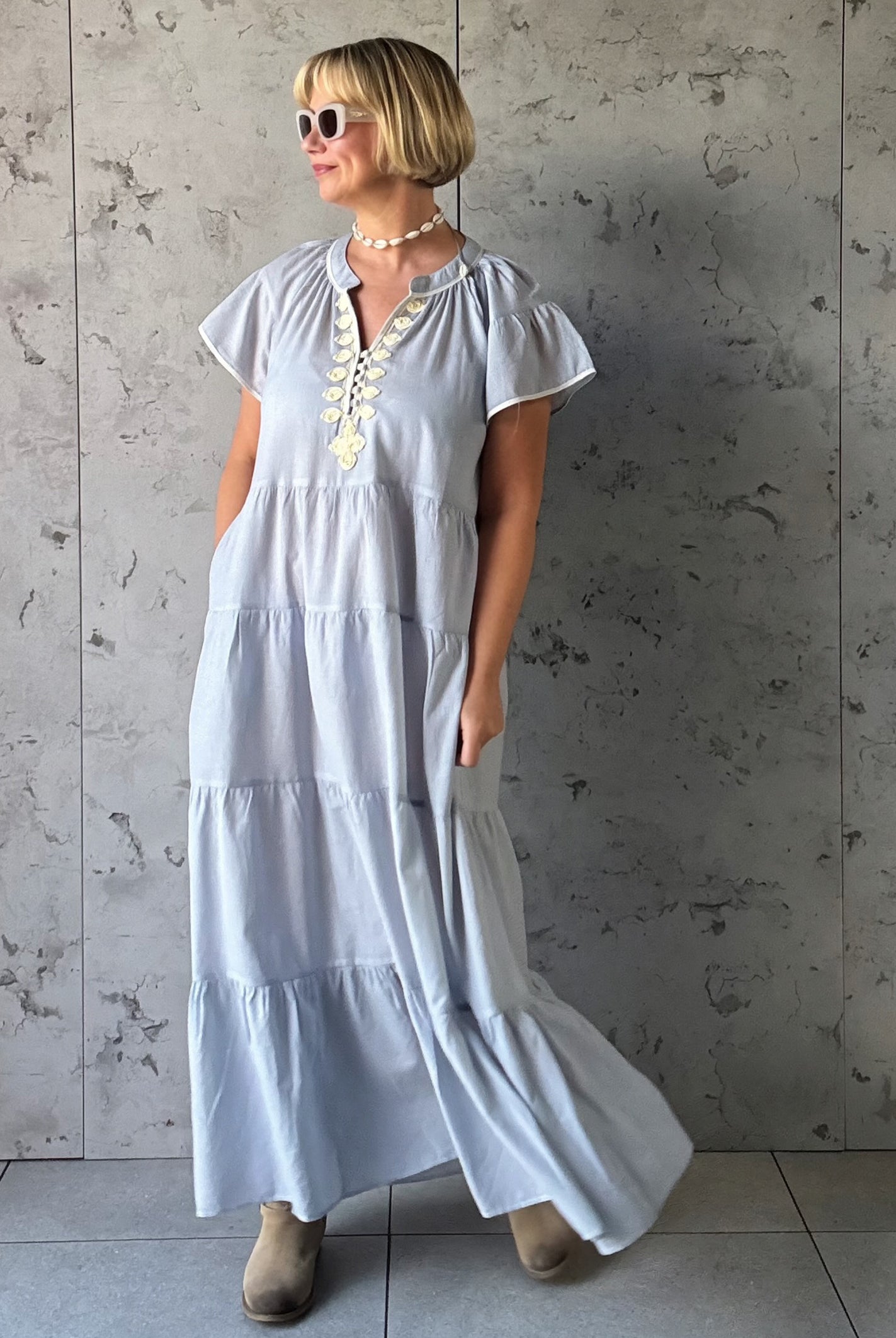 Woman wearing a blue striped dress against a gray concrete wall.