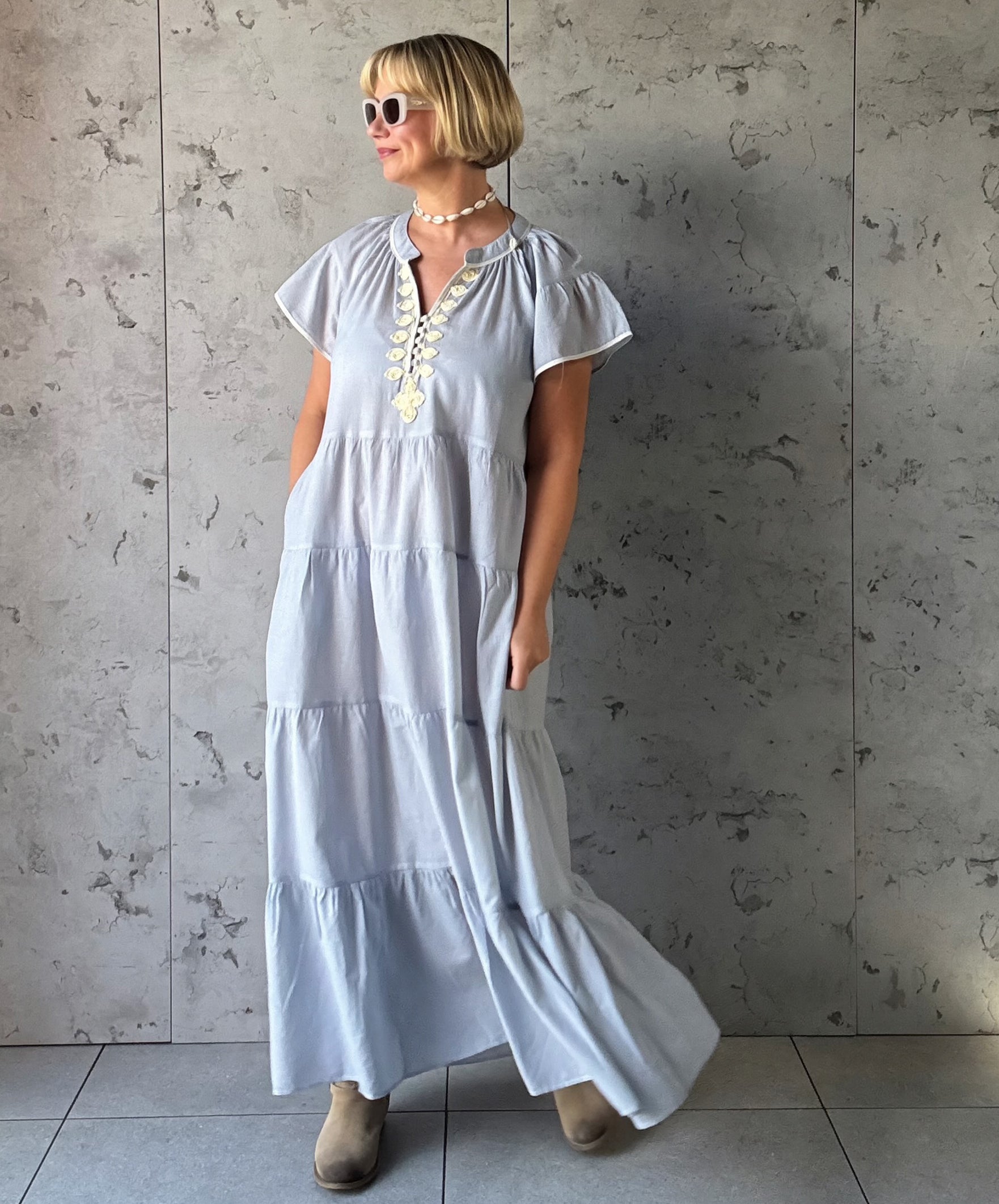 Woman wearing a blue striped dress against a gray concrete wall.
