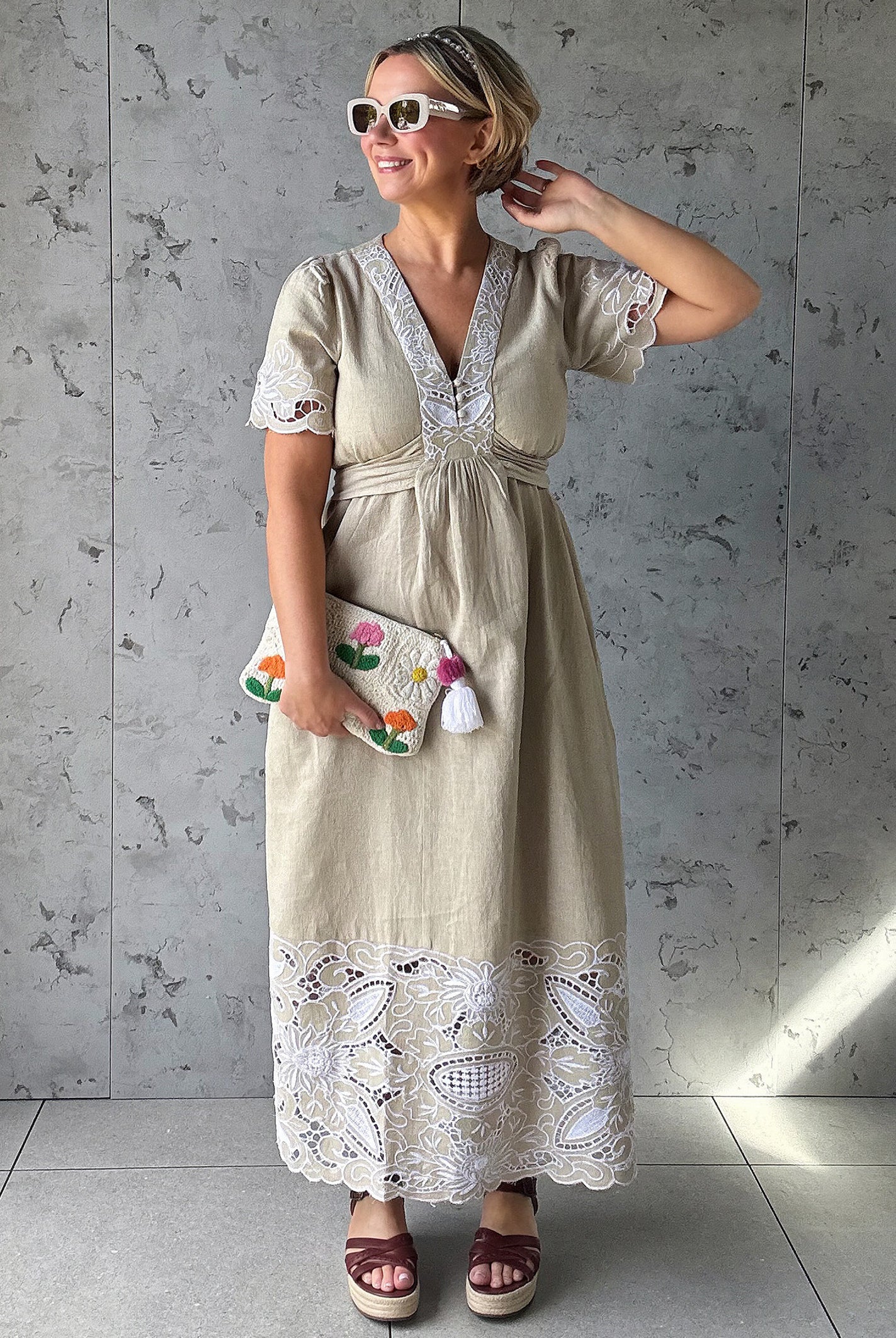 Influencer @rosemaejewel wearing a Hawthorn natural dress with lace embroidery details holding a colorful handbag against a gray concrete wall.