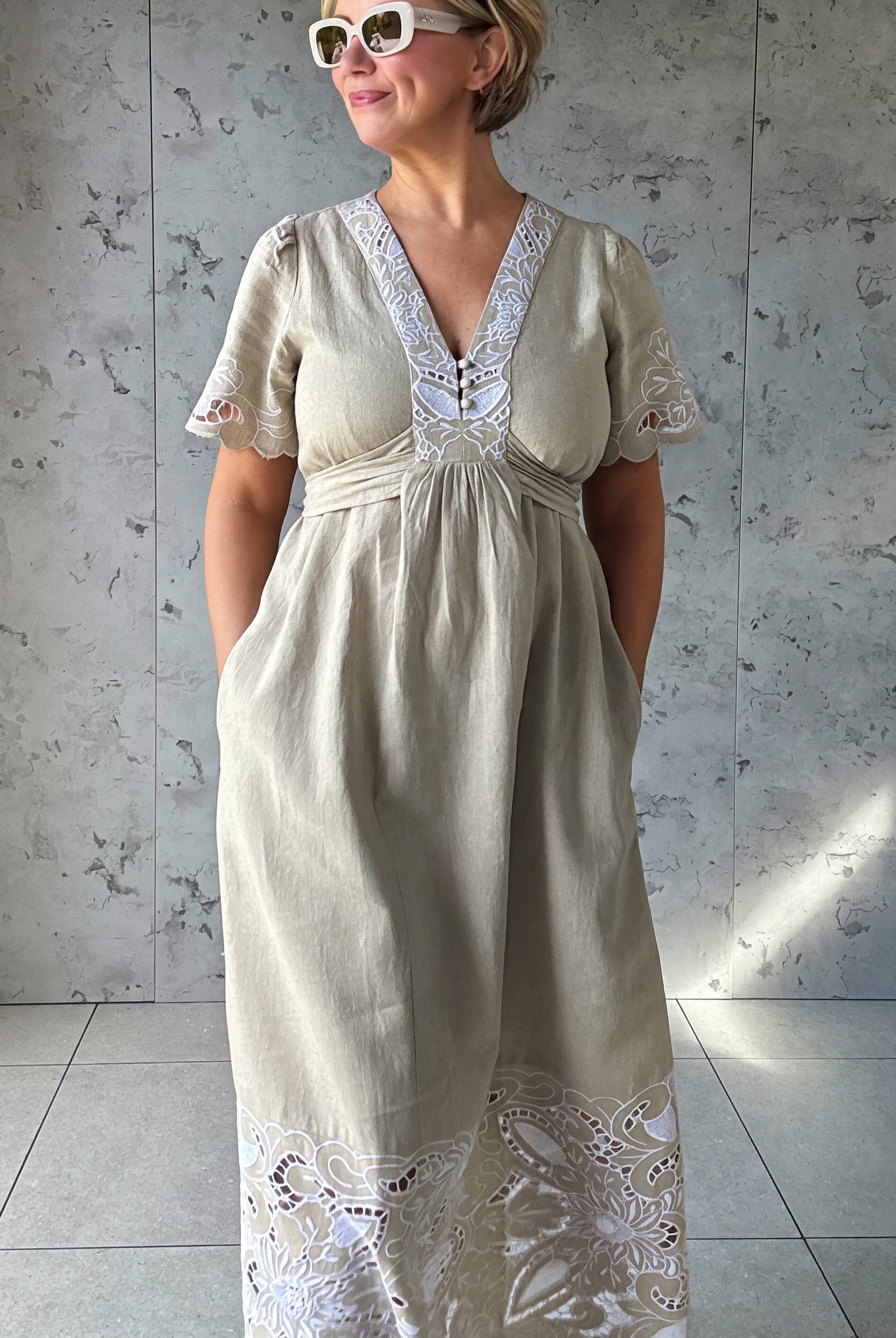 Influencer @rosemaejewel wearing a Hawthorn natural dress with her hands in the pockets against a gray concrete wall.