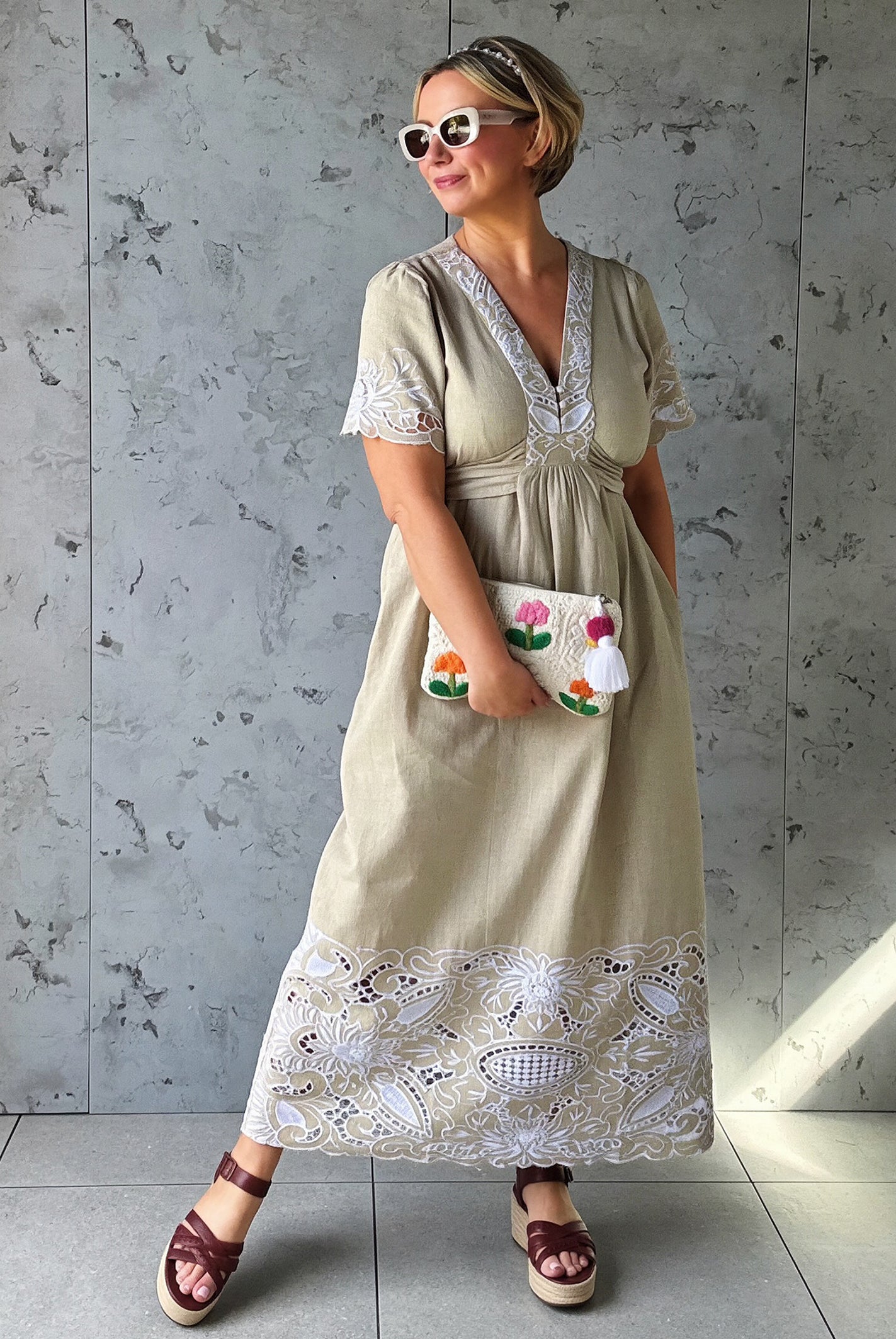 Influencer @rosemaejewel wearing a Hawthorn natural dress with lace embroidery details holding a colorful handbag against a gray concrete wall.