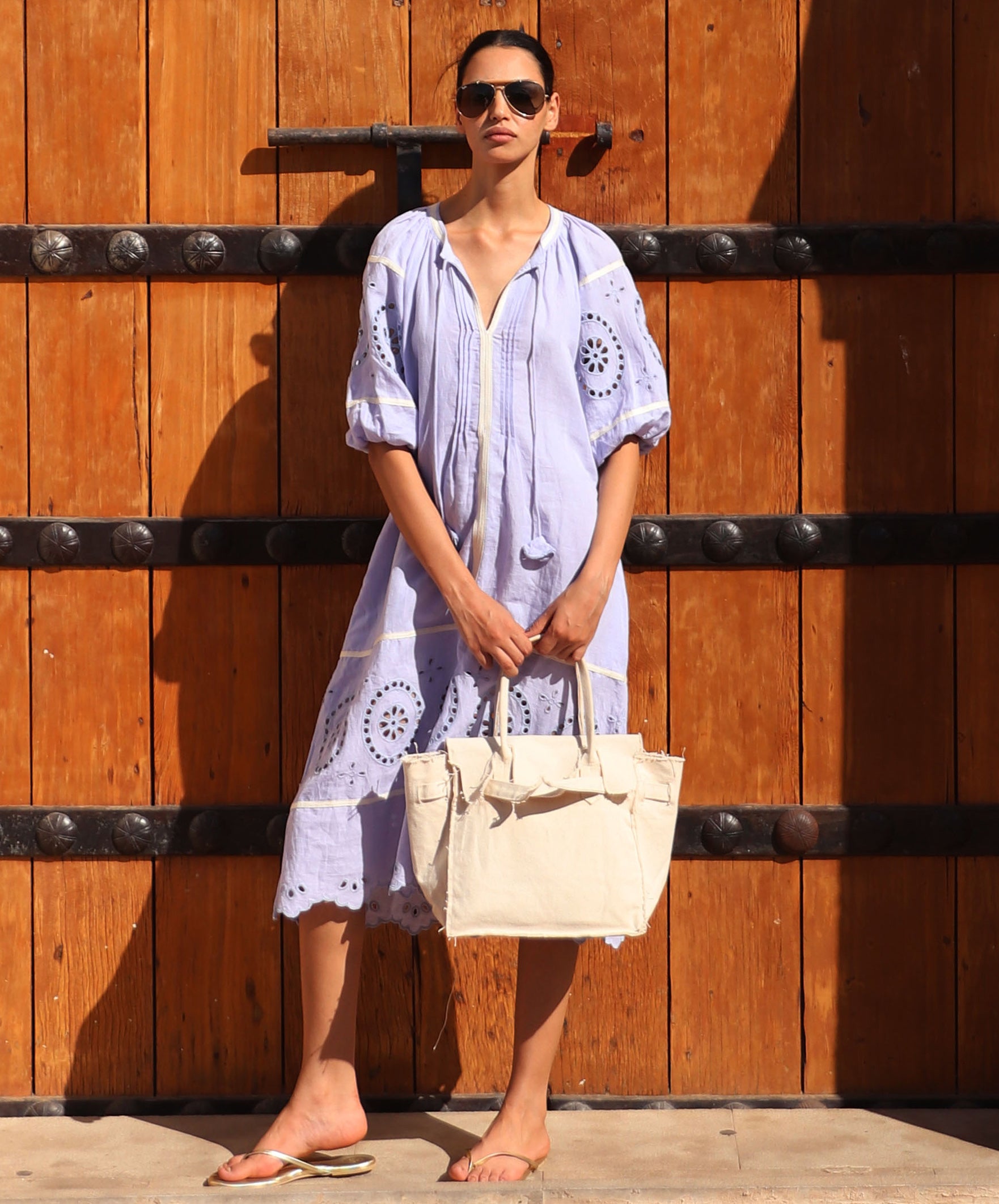 Woman in a light blue dress holding a cream bag against a wooden background