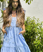 A model stood in a garden wearing a Rose and Rose blue cotton Marina sundress.