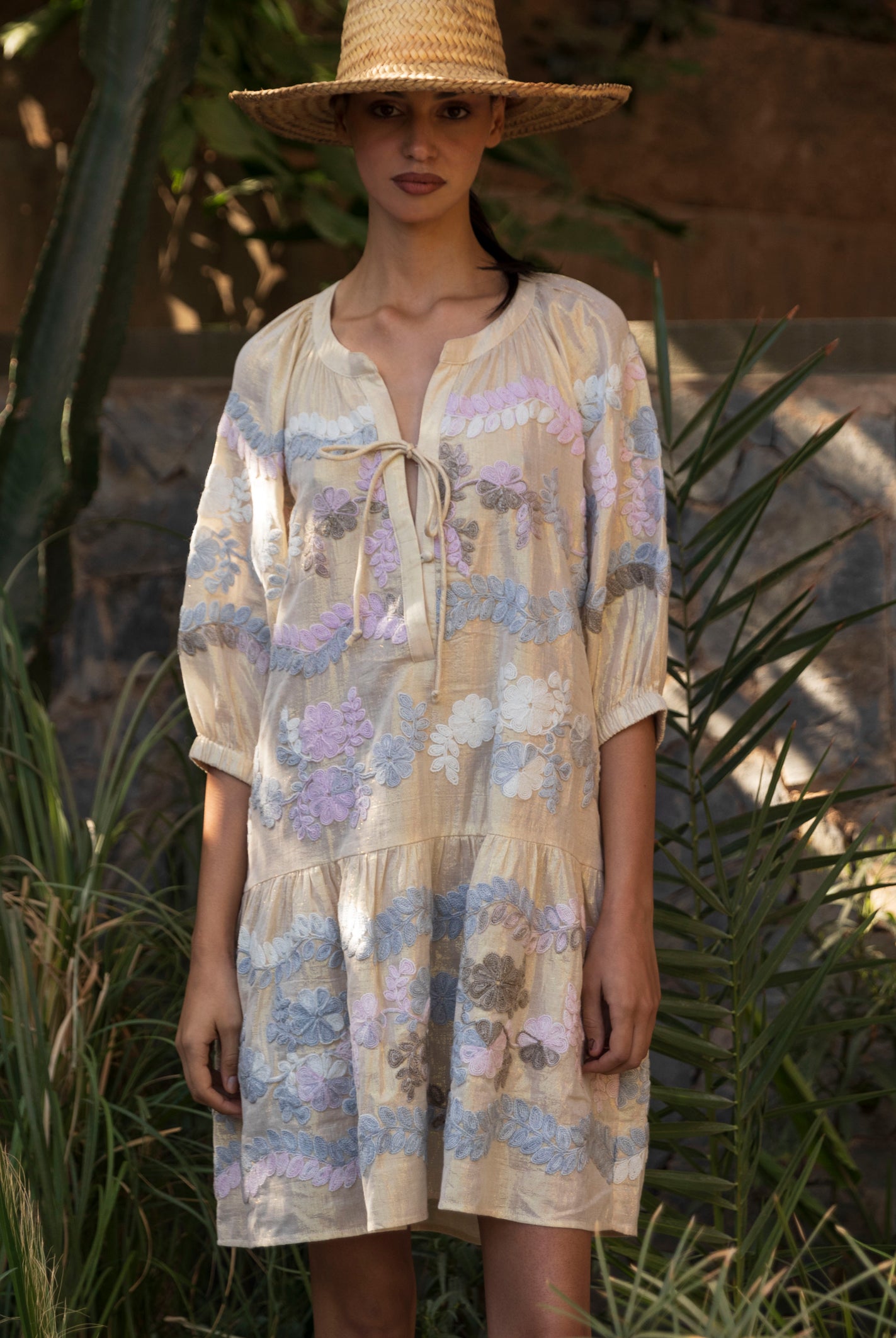 Woman wearing a floral embroidered gold Oleander dress and straw hat in a tropical garden