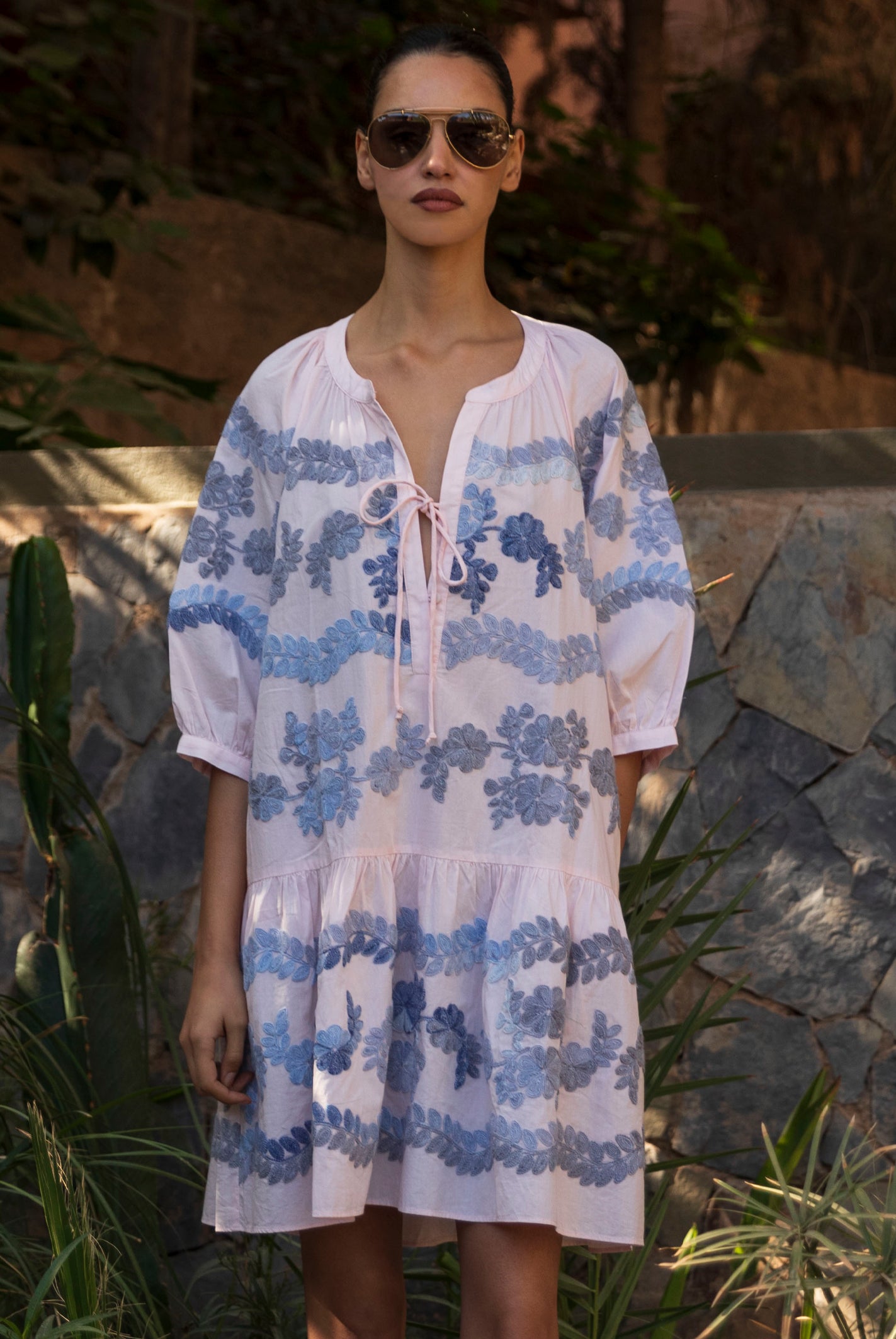 Woman wearing a light pink Oleander dress with blue floral embroidery pattern.