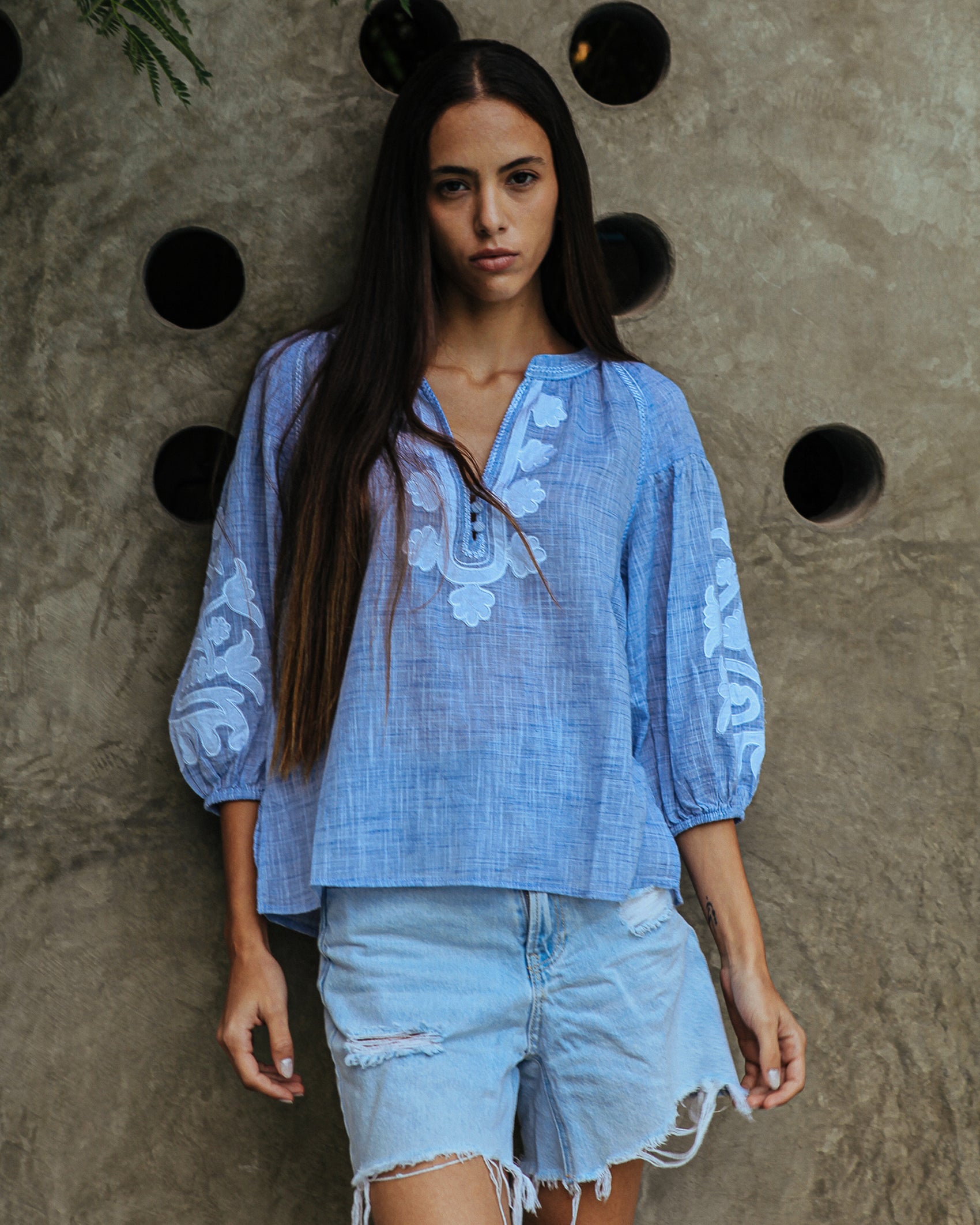 A model is wearing a Rose and Rose Oval top in blue slub with white appliqué decoration.