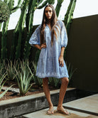 A model stood in a cacti garden wearing a Rose and Rose Oxford dress in marl blue with white appliqué decoration.