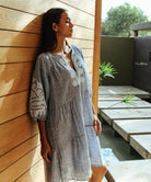 A model wearing a Rose and Rose Oxford dress in marl blue with white appliqué decoration.