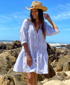 A model on a beach wearing a cowboy hat and a Rose and Rose pale blue cotton embroidered Palermo dress.