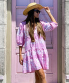 A model wearing sunglasses and a cowboy hat stood in front of a pink door wearing a Rose and Rose pale pink Palermo embroidered dress. 