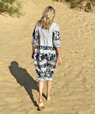 Back view of a model walking along a beach wearing a Rose and Rose striped linen Portafino dress.