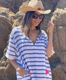 A close up of a model standing on the beach wearing a Rosebud by Rose and Rose Aix beach dress, sunglasses and hat. 