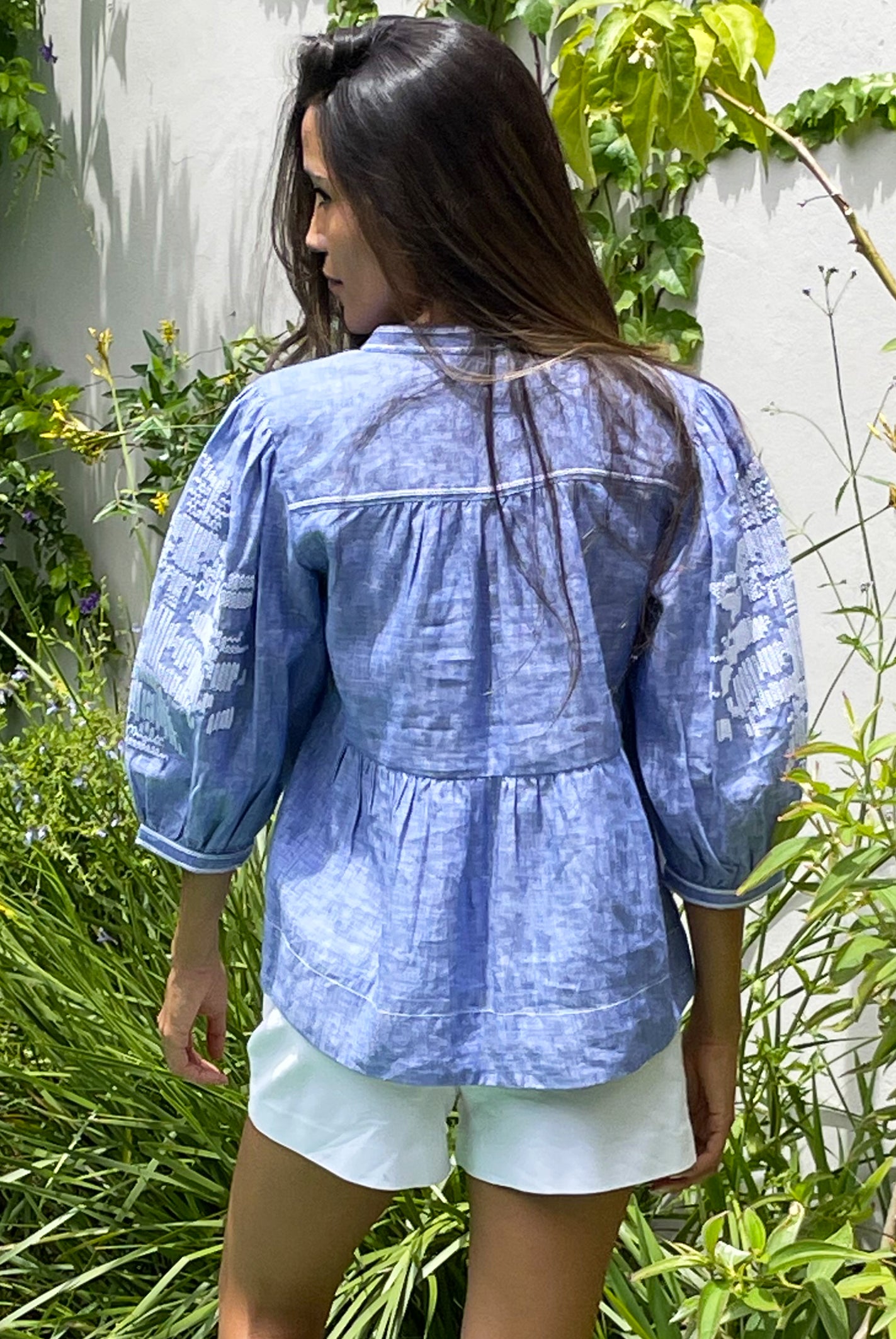 Back view of a model wearing the blue chambray linen Rose and Rose Sardinia top and white shorts.