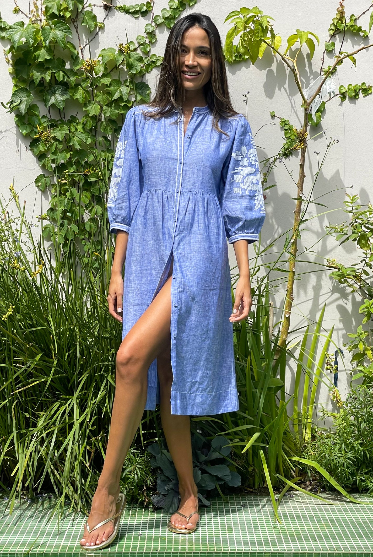 A model in a garden wearing a Rose and Rose blue linen Sicily dress.
