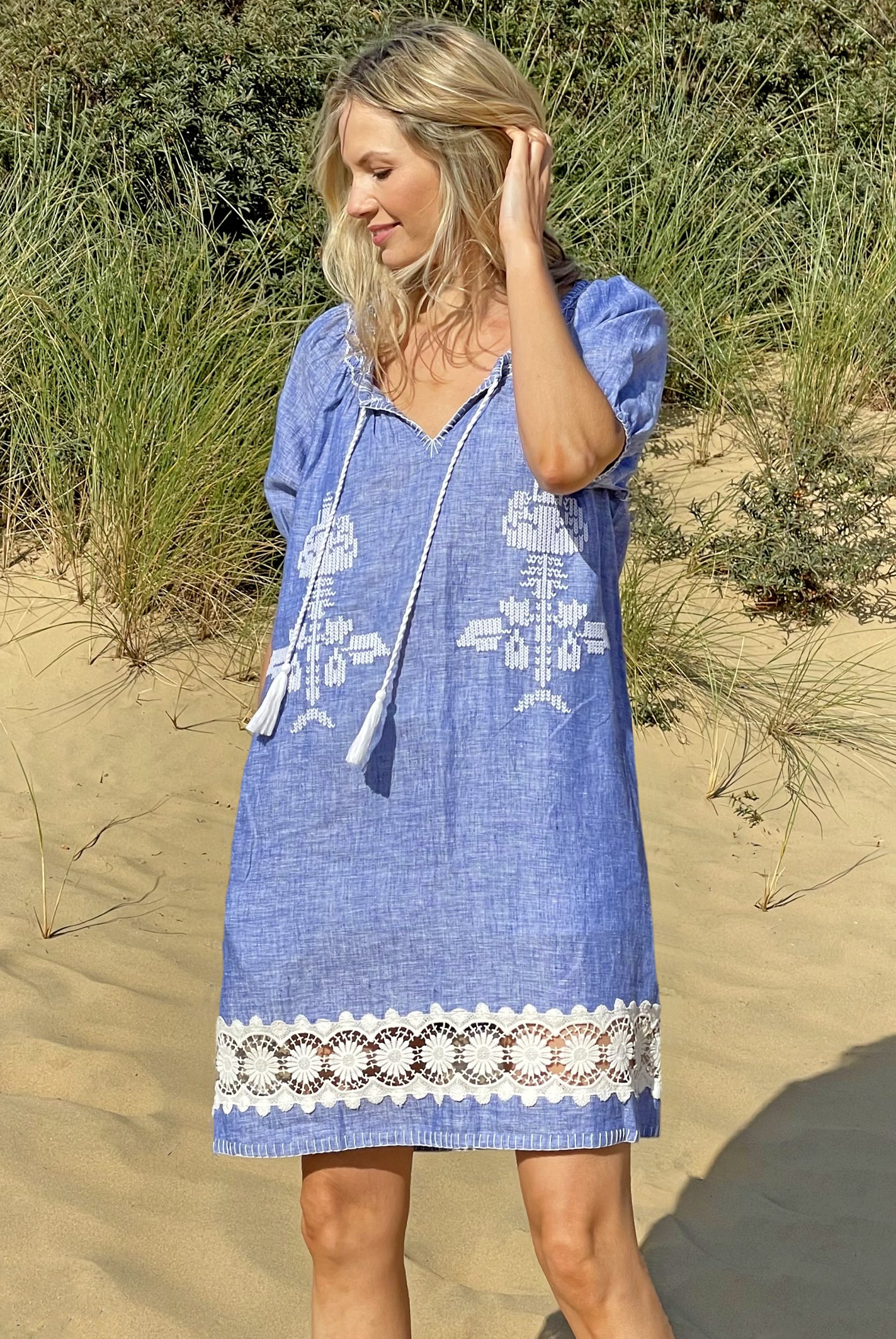 A model on a beach wearing the Rose and Rose Siracusa embroidered blue linen dress.