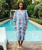 A model stood in front of a swimming pool wearing a Rose and Rose Snaresbrook striped cotton dress with white embroidery.