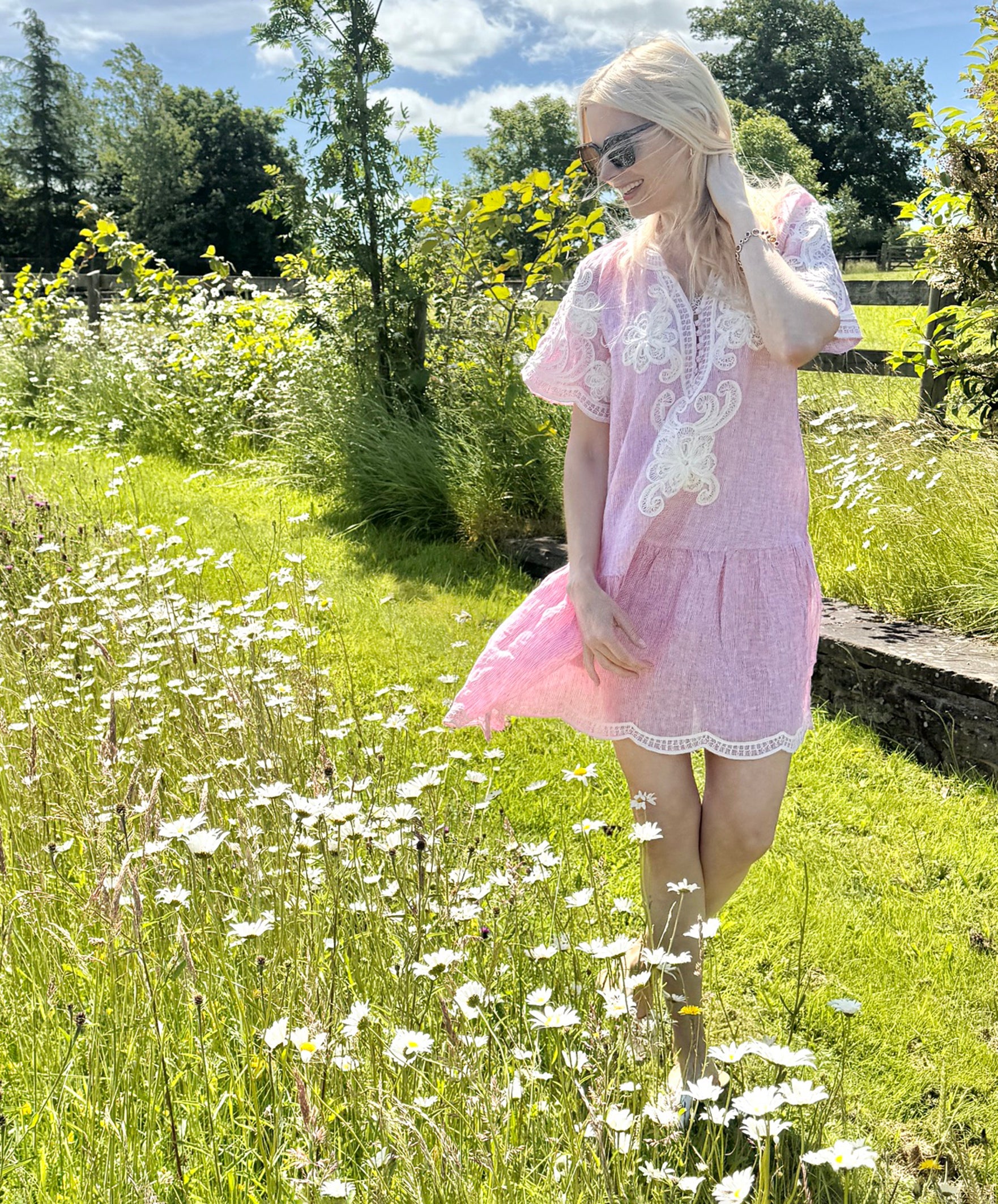 Influencer @swedishgirlinlondon wearing the Amaranta red striped dress with white decoration walking in a meadow.