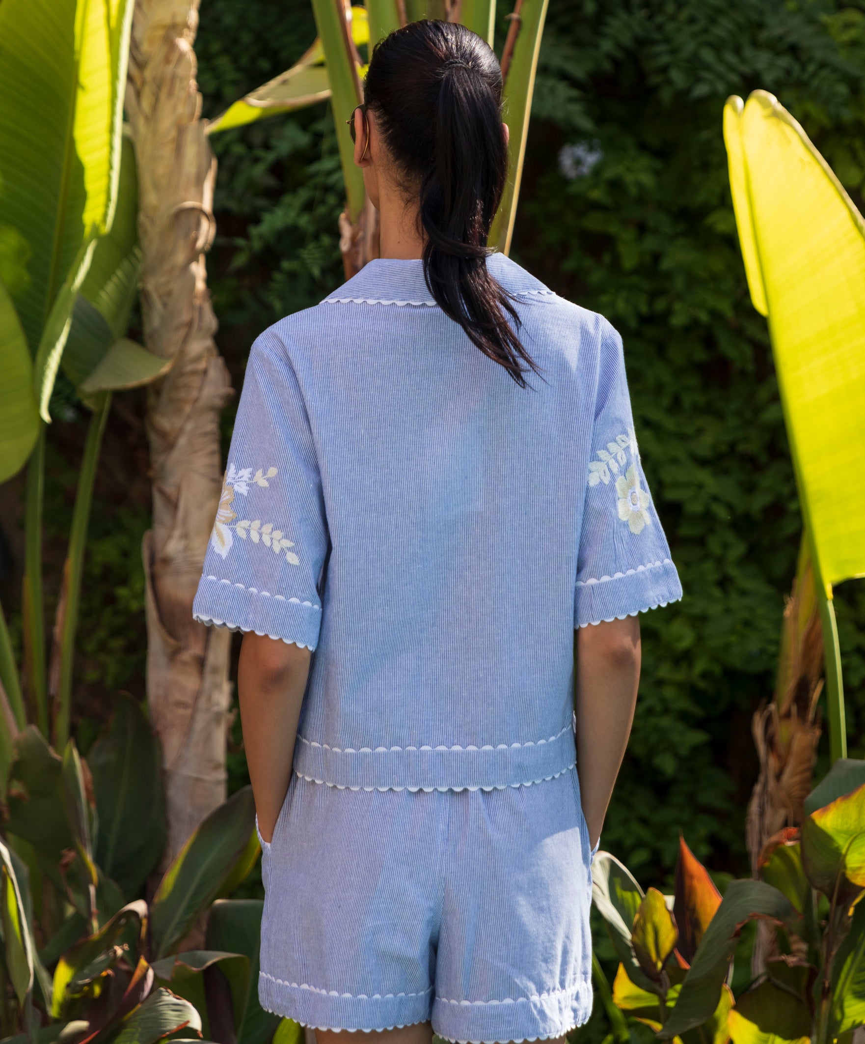 Back view of a woman wearing a blue striped shirt with matching shorts in a garden setting