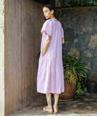 A side view of a model wearing a Rose and Rose Uxbridge dress in pink with berry passementerie decoration.