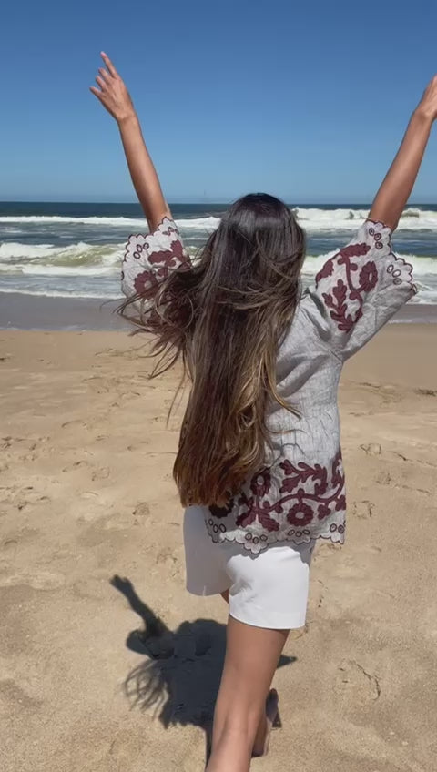 a model on a beach skipping and waving her arms about in glee, wearing a Rose and Rose Alessio top and white shorts.