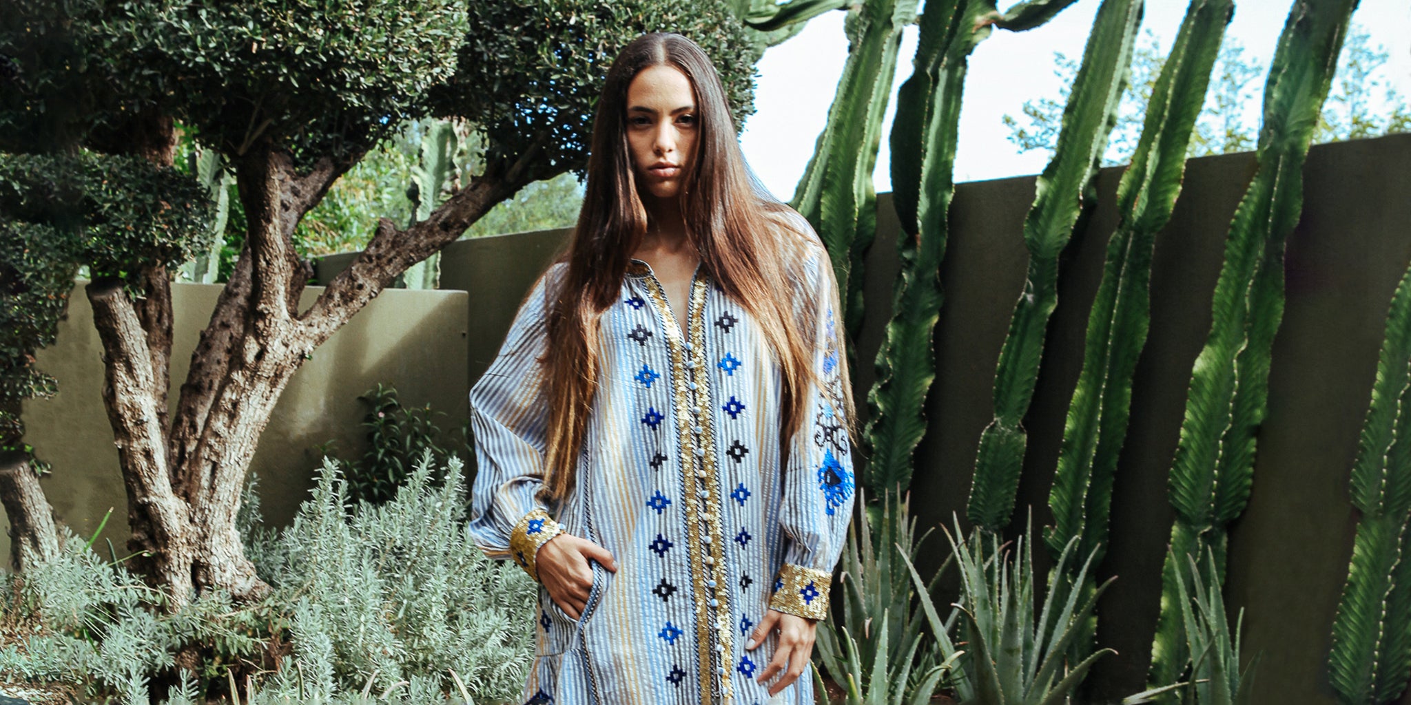 A model stood in a cacti garden wearing a Rose and Rose Temple striped dress with sequin and embroidery decoration.