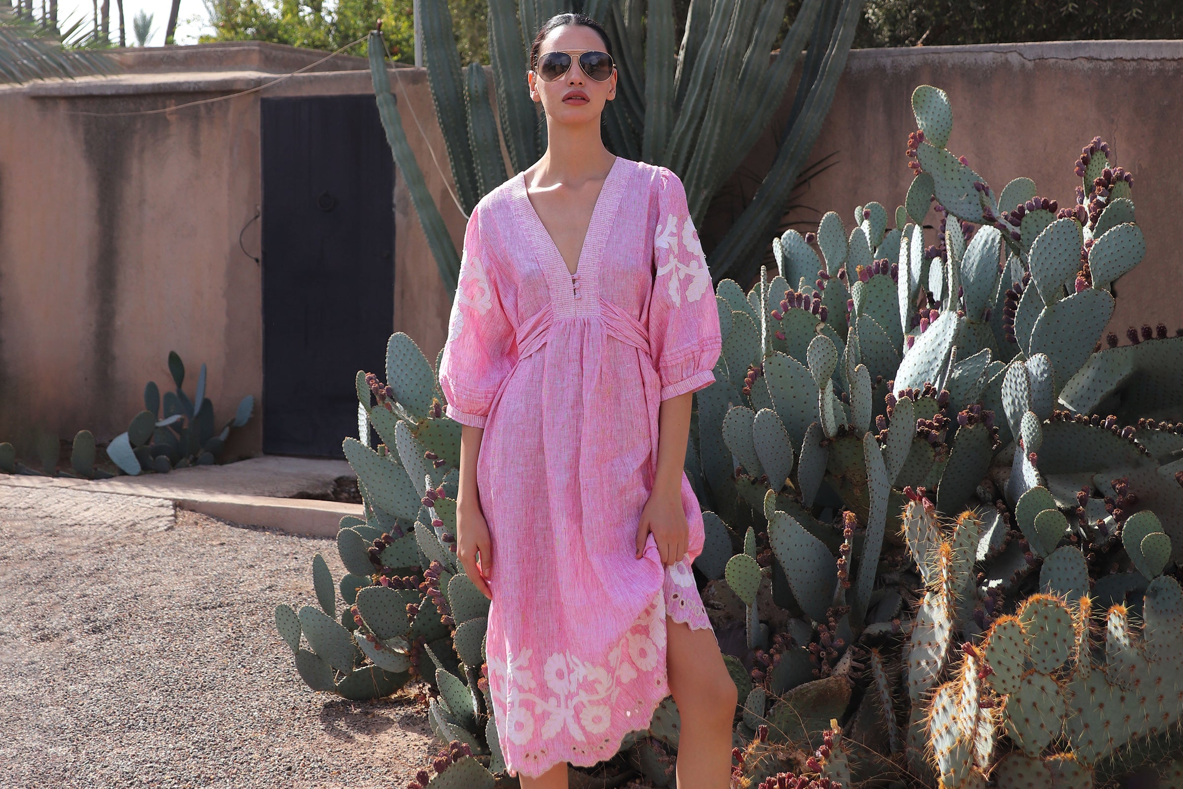 Woman in a red striped dress with floral decoration and embroidery standing among cacti
