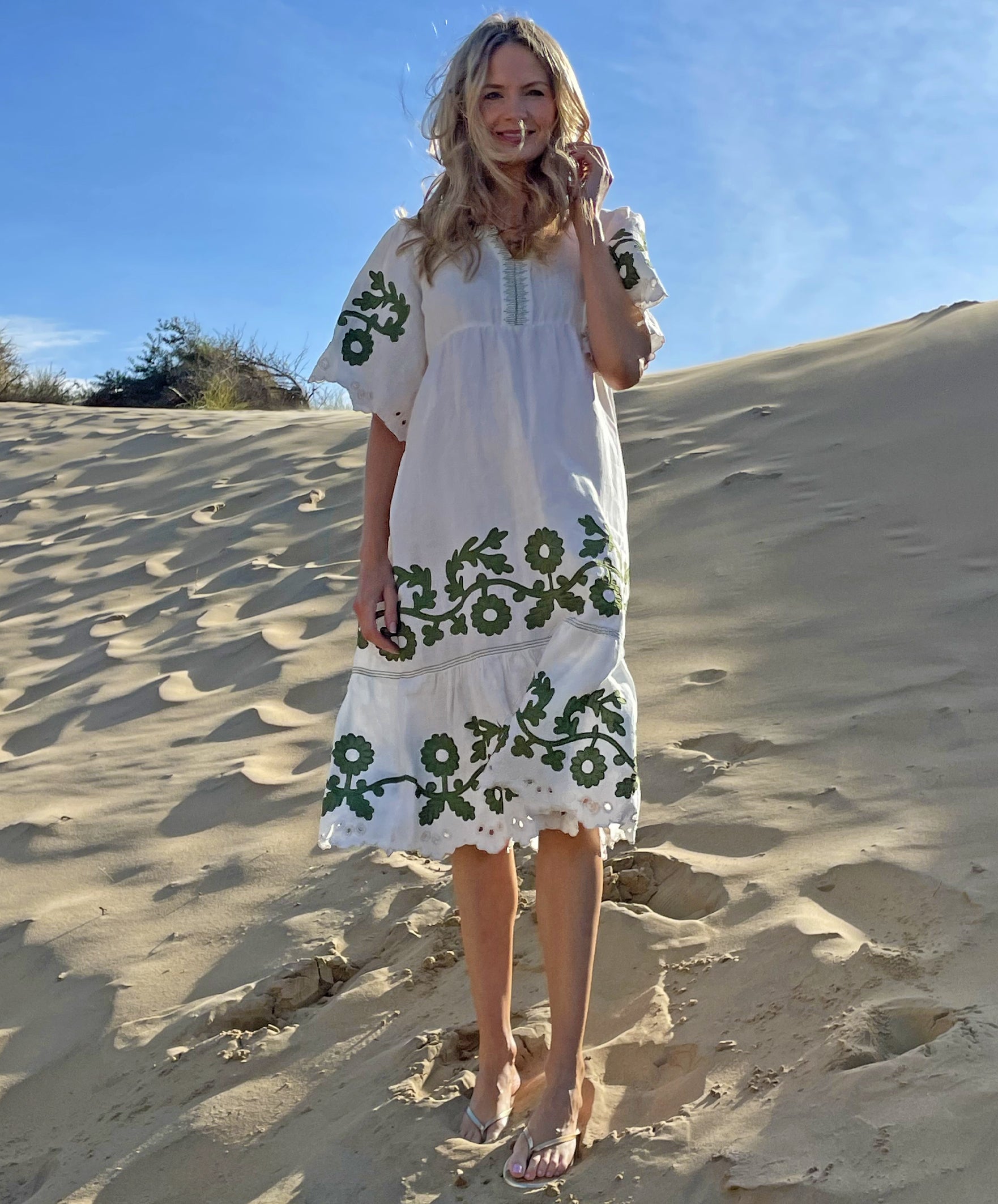 A model on a beach wearing the Rose and Rose Agrigento dress in white linen with olive applique.
