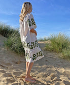 A back view of a model on a beach wearing the Rose and Rose Agrigento dress in white linen with olive applique.