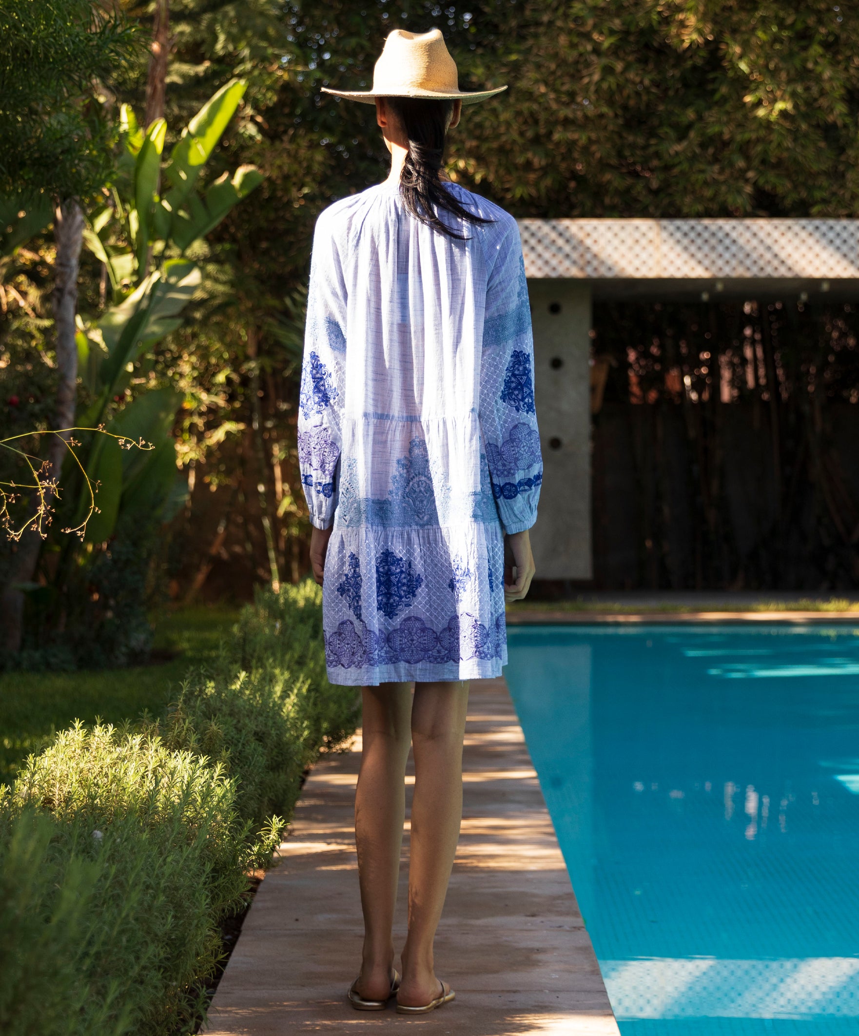 Back view of a woman wearing the Alder blue floral embroidered dress stood next to a pool.