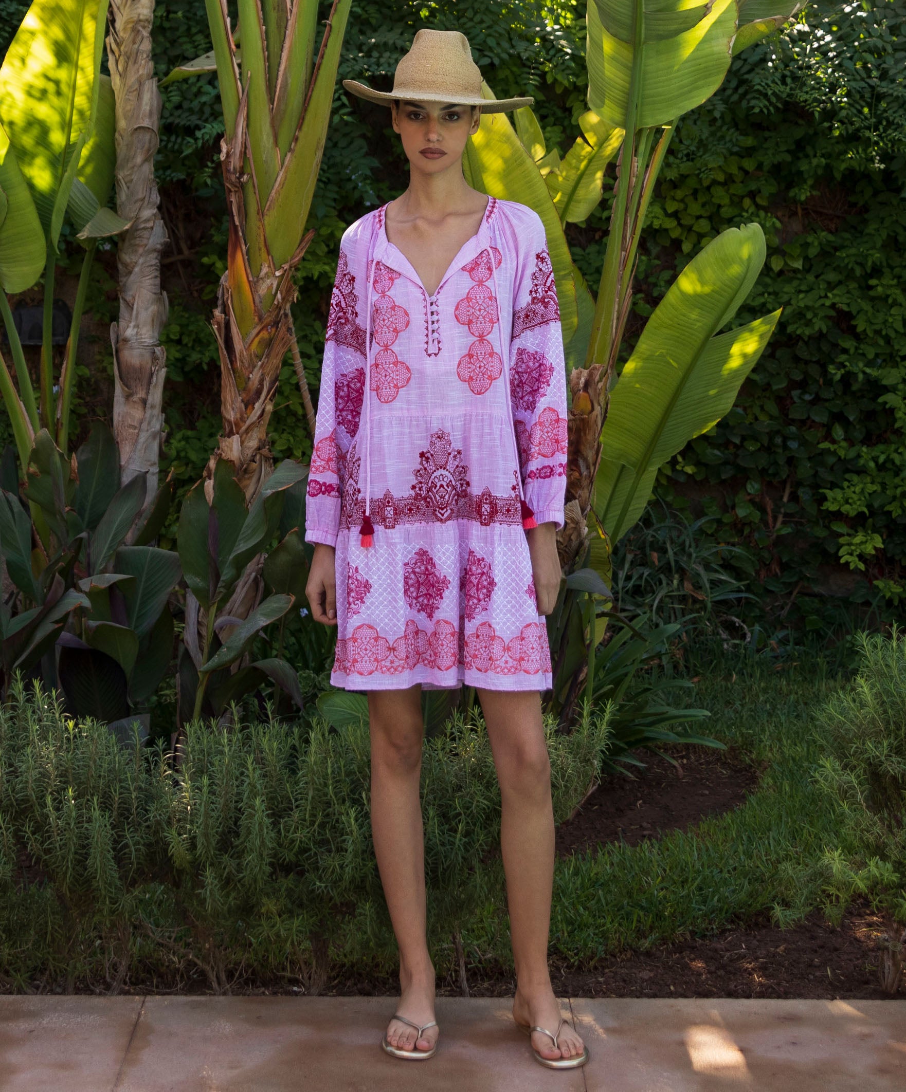 Woman wearing an Alder pink floral embroidered dress standing in a tropical garden setting