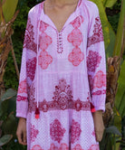 Close up of model wearing a pink and red embroidered Alder dress with tassels in a tropical setting.