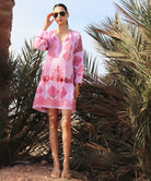 Woman in a pink embroidered Alder dress standing among palm trees