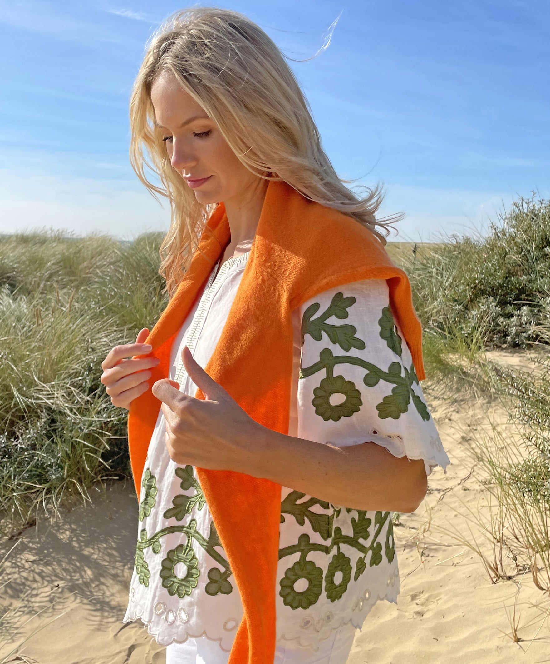 A model on a beach wearing the Rose and Rose Alessio top in white linen with olive applique and a Jumper 1234 jumper over her shoulders.