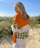 A back view of a model on a beach wearing the Rose and Rose Alessio top in white linen with olive applique and a Jumper 1234 jumper over her shoulders.