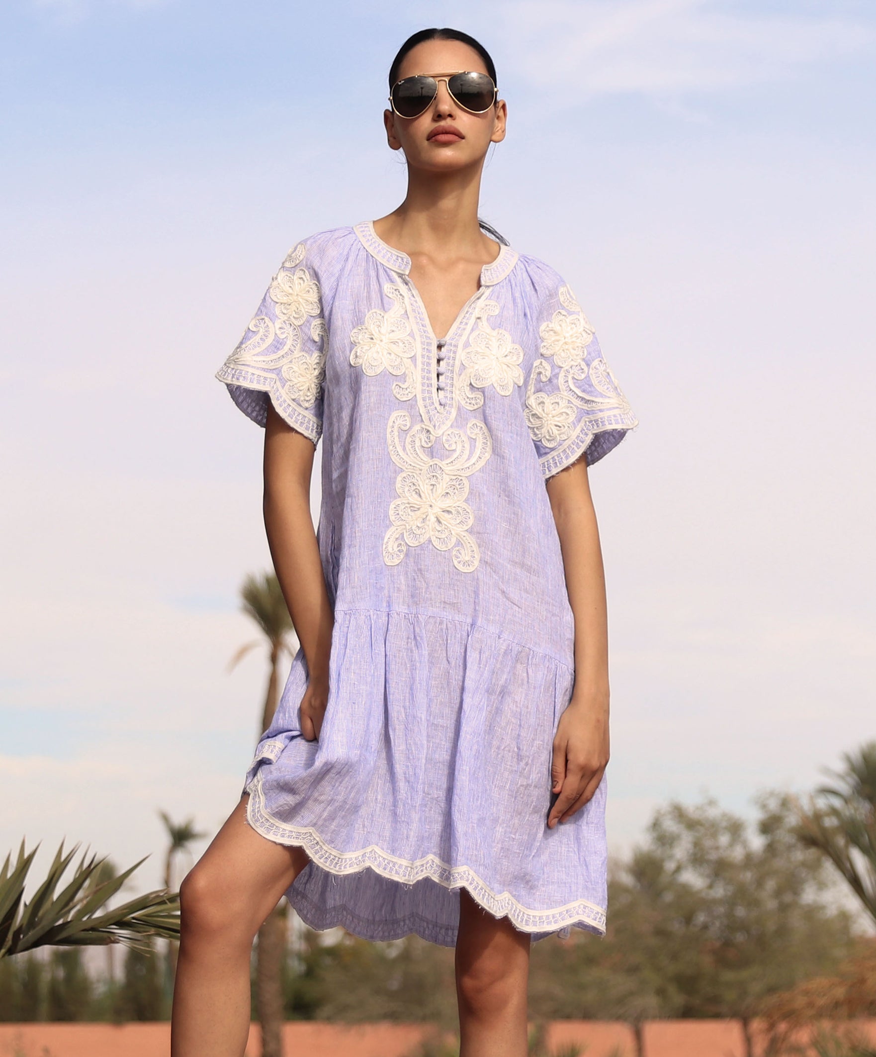 Woman wearing a striped blue Amaranta dress with white tape decoration with sunglasses against a desert background