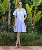 Woman in a blue striped Amaranta dress with tapework decoration standing in a tropical garden.